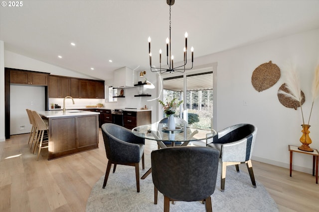 dining area featuring lofted ceiling, sink, light hardwood / wood-style floors, and a chandelier