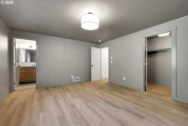 unfurnished bedroom featuring a walk in closet, ensuite bath, a textured ceiling, light wood-type flooring, and a closet