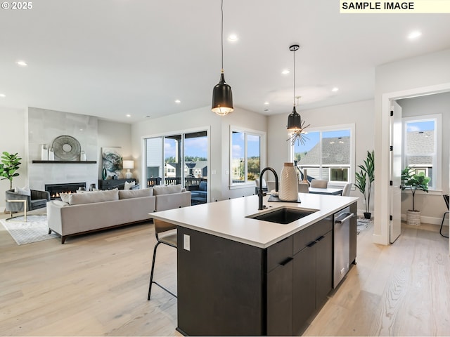 kitchen featuring a fireplace, sink, hanging light fixtures, a kitchen island with sink, and light hardwood / wood-style flooring