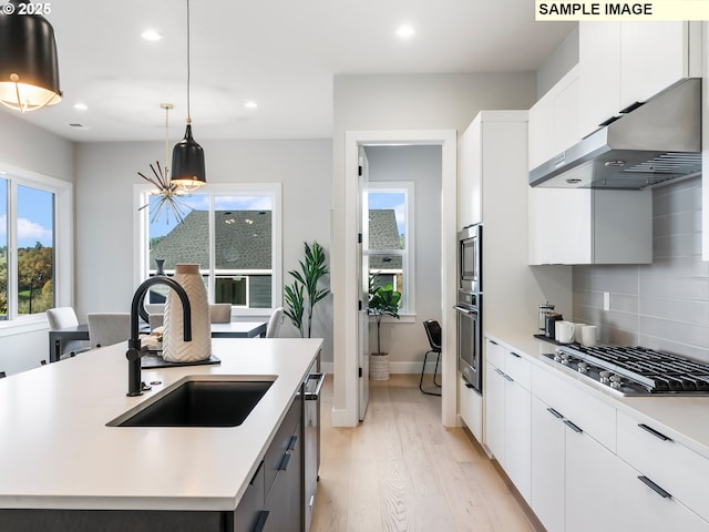 kitchen with pendant lighting, sink, white cabinetry, extractor fan, and an island with sink