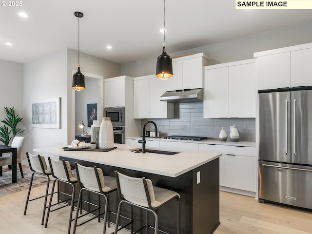 kitchen featuring white cabinetry, stainless steel appliances, decorative light fixtures, and a kitchen island with sink