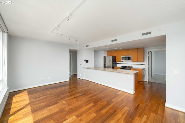 kitchen featuring sink, stainless steel appliances, wood-type flooring, track lighting, and kitchen peninsula