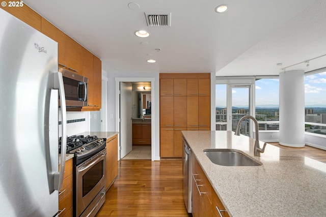 kitchen with sink, light stone counters, track lighting, appliances with stainless steel finishes, and hardwood / wood-style floors