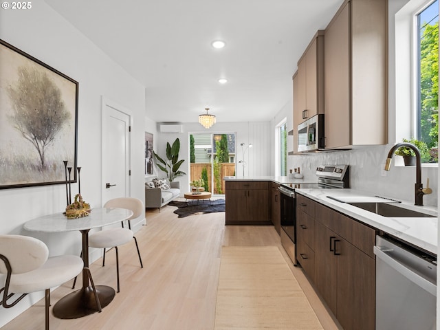 kitchen with a wall mounted AC, a sink, light countertops, light wood-style floors, and stainless steel appliances