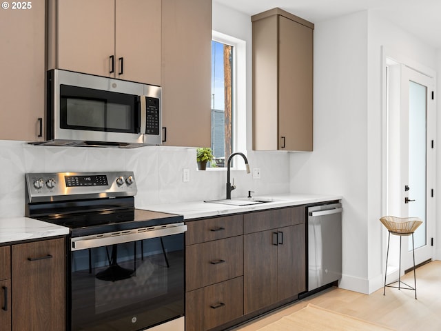 kitchen with backsplash, light stone countertops, a sink, light wood finished floors, and stainless steel appliances