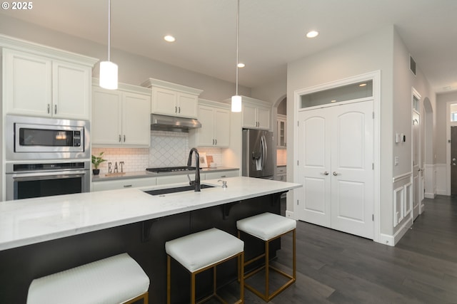 16922 NW Madrone St, Portland, OR 97229 - kitchen featuring stainless steel appliances, under cabinet range hood, a sink, arched walkways, and tasteful backsplash
