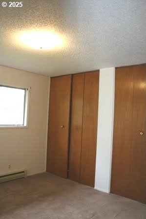 14737 SW Hall Blvd, Tigard, OR 97224 - unfurnished bedroom featuring a baseboard radiator, a textured ceiling, two closets, and carpet flooring