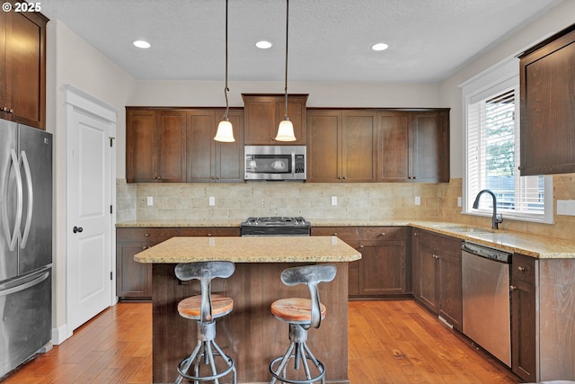 14670 SW 78th Ave, Tigard, OR 97224 - kitchen with appliances with stainless steel finishes, a sink, light wood-style flooring, a center island, and light stone counters