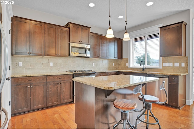 14670 SW 78th Ave, Tigard, OR 97224 - kitchen featuring stainless steel appliances, a sink, light wood-type flooring, light stone countertops, and recessed lighting