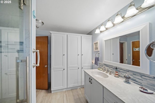 bathroom featuring vanity, decorative backsplash, a shower with shower door, and hardwood / wood-style flooring