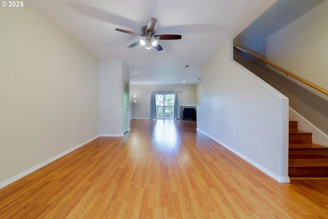 unfurnished living room featuring stairway, light wood-style floors, a ceiling fan, and a fireplace