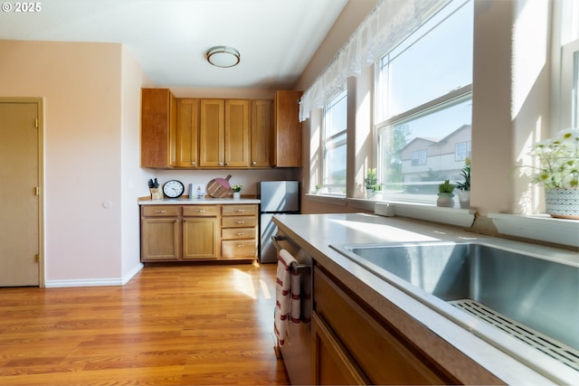 kitchen featuring freestanding refrigerator, brown cabinetry, light wood-style flooring, light countertops, and dishwashing machine