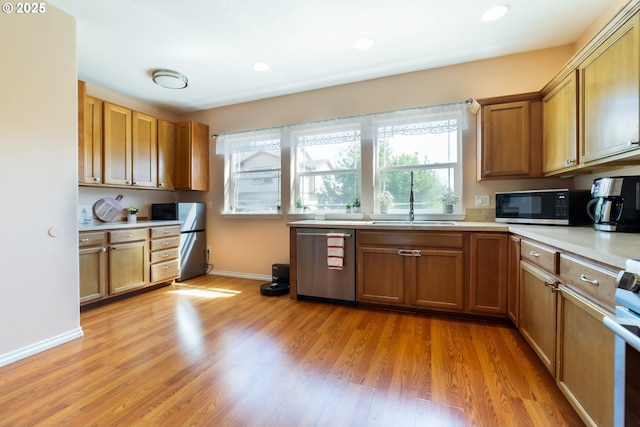 kitchen featuring stainless steel appliances, a sink, light countertops, light wood-style flooring, and brown cabinets