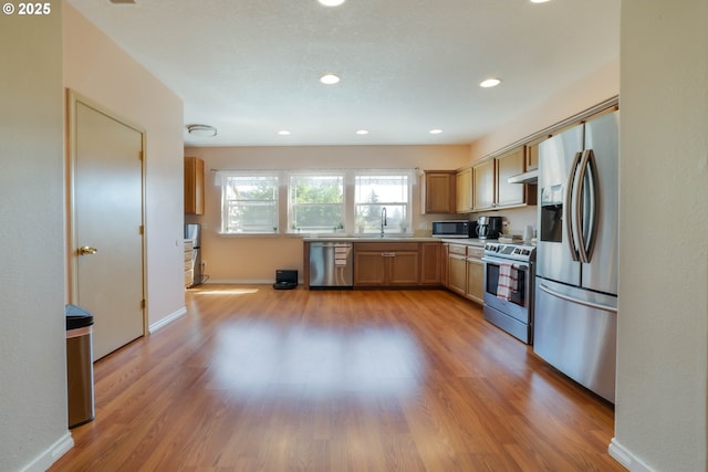 kitchen with appliances with stainless steel finishes, light wood finished floors, light countertops, a sink, and recessed lighting