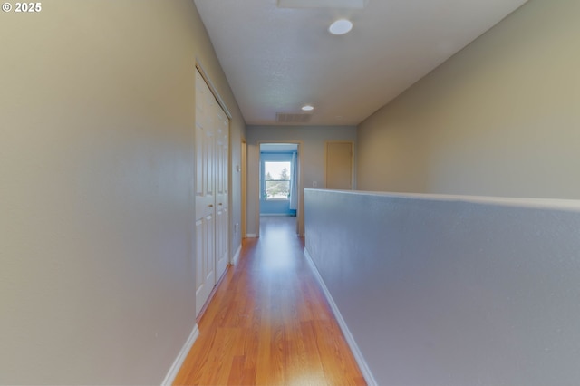corridor with baseboards, light wood-type flooring, and an upstairs landing