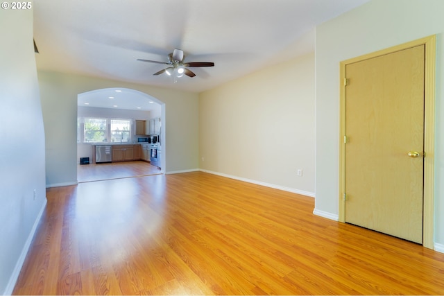 unfurnished living room with ceiling fan, arched walkways, light wood-style flooring, and baseboards