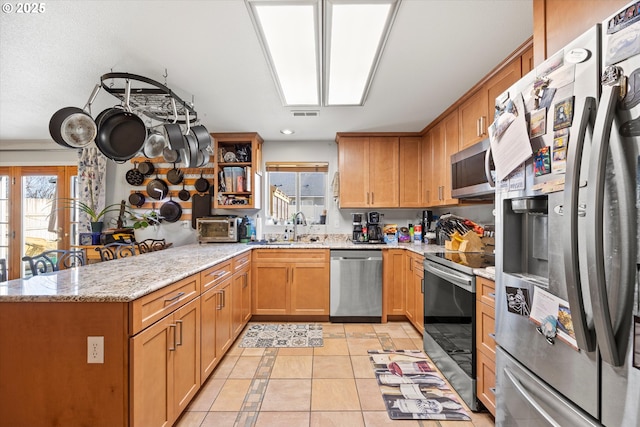 kitchen with appliances with stainless steel finishes, sink, light tile patterned floors, light stone counters, and kitchen peninsula