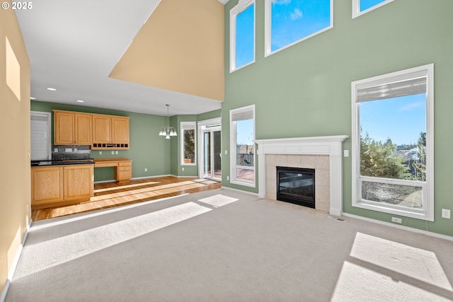 unfurnished living room featuring a towering ceiling, a tiled fireplace, light carpet, and a chandelier