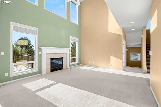 unfurnished living room featuring a high ceiling, a tile fireplace, and light carpet