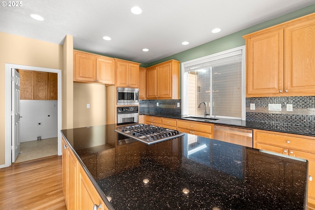 kitchen featuring appliances with stainless steel finishes, dark stone counters, sink, light hardwood / wood-style flooring, and tasteful backsplash