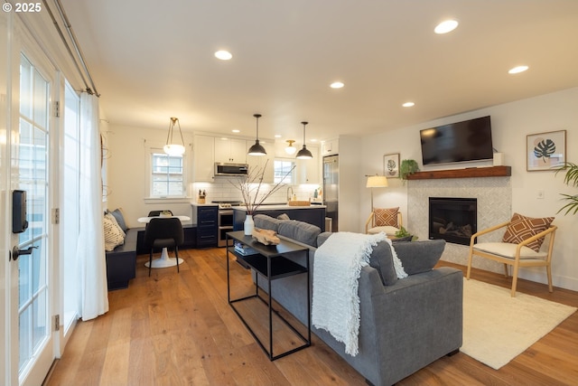 living room featuring baseboards, recessed lighting, a tiled fireplace, and light wood-style floors