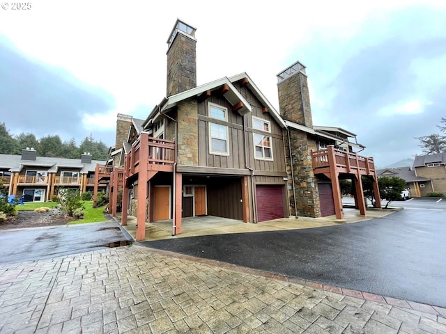 view of front of home featuring a chimney, an attached garage, board and batten siding, stone siding, and a wooden deck