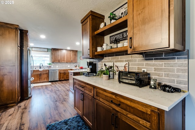 kitchen with sink, stainless steel appliances, tasteful backsplash, wood-type flooring, and light stone countertops