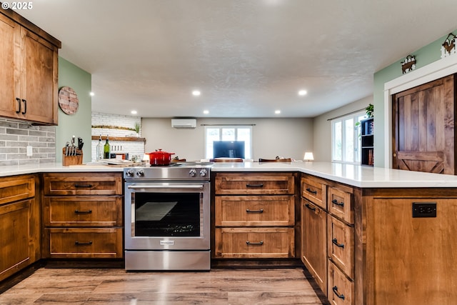 kitchen featuring light hardwood / wood-style flooring, kitchen peninsula, a wall unit AC, high end stove, and backsplash