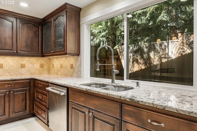kitchen with dark brown cabinets, light stone countertops, tasteful backsplash, a sink, and dishwasher