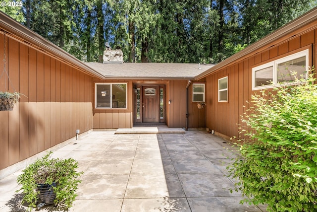 entrance to property with a shingled roof, board and batten siding, and a chimney