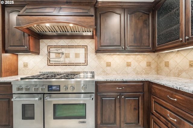 kitchen with custom range hood, dark brown cabinets, double oven range, and tasteful backsplash