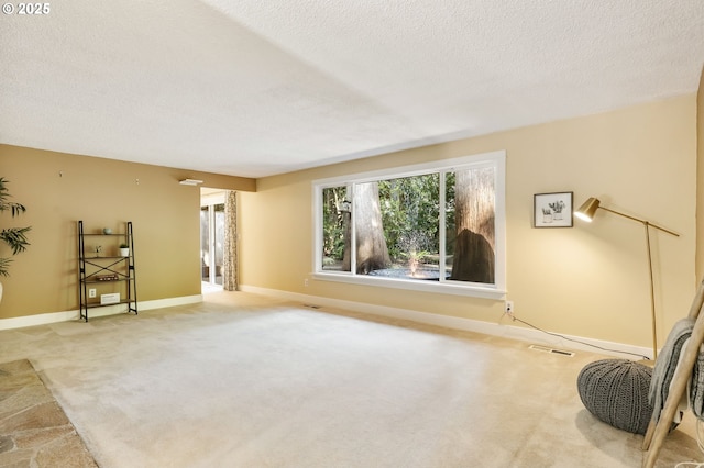 interior space with baseboards, light colored carpet, a textured ceiling, and visible vents