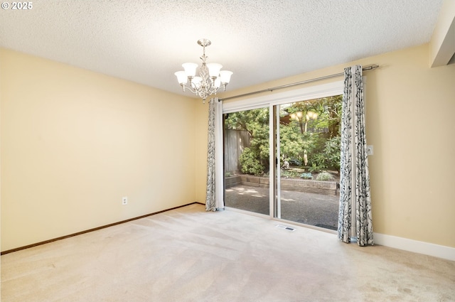carpeted spare room with a textured ceiling, baseboards, a notable chandelier, and visible vents