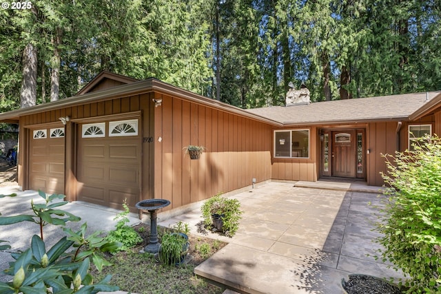 view of front of property with a garage, board and batten siding, a chimney, and roof with shingles