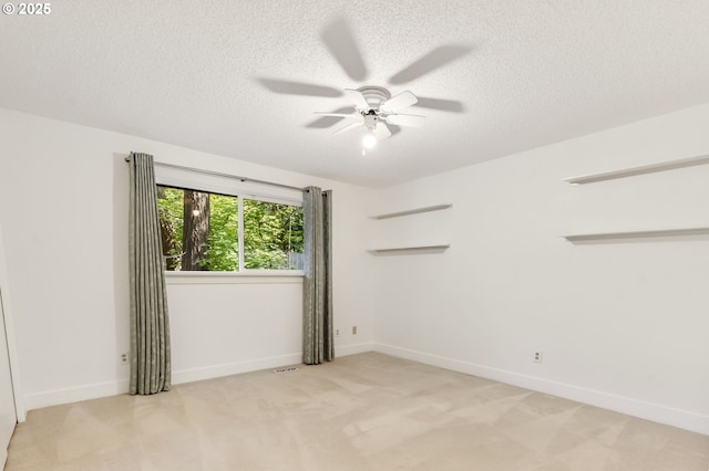 spare room with ceiling fan, a textured ceiling, visible vents, baseboards, and light carpet
