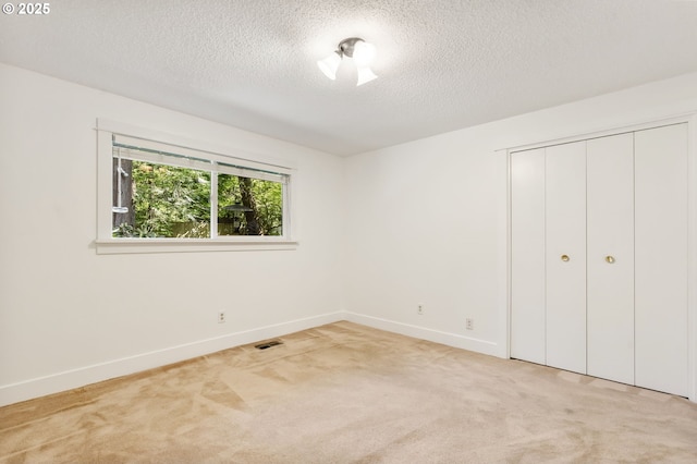 unfurnished bedroom with light colored carpet, a textured ceiling, visible vents, and baseboards