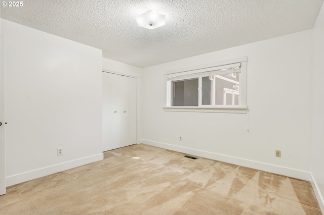unfurnished room with visible vents, carpet, a textured ceiling, and baseboards
