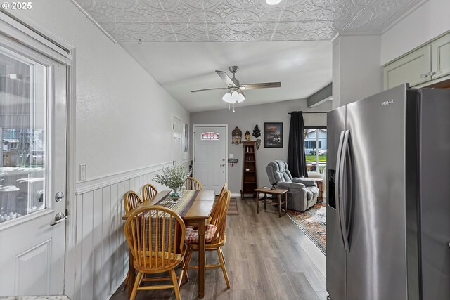 dining area featuring a ceiling fan, light wood-style flooring, and wainscoting