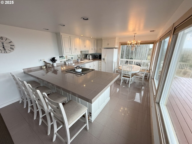 kitchen featuring tile countertops, decorative light fixtures, a peninsula, white fridge with ice dispenser, and white cabinetry