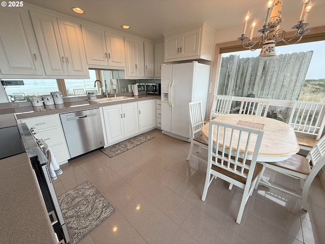 kitchen featuring white refrigerator with ice dispenser, decorative light fixtures, stainless steel dishwasher, white cabinets, and a sink