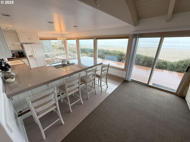 dining area featuring light tile patterned floors, a chandelier, recessed lighting, a water view, and beam ceiling