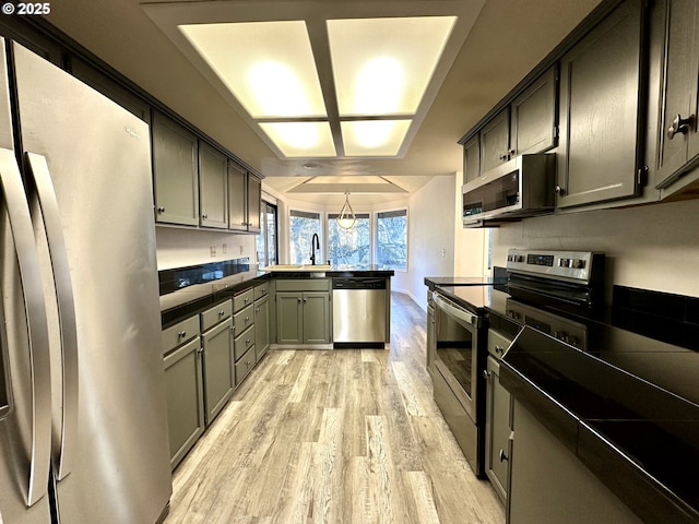 kitchen featuring appliances with stainless steel finishes, kitchen peninsula, sink, and light hardwood / wood-style flooring