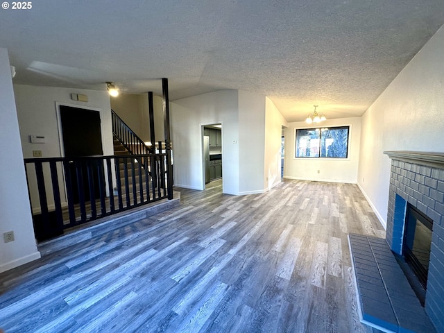 unfurnished living room featuring lofted ceiling, a chandelier, a brick fireplace, a textured ceiling, and hardwood / wood-style flooring