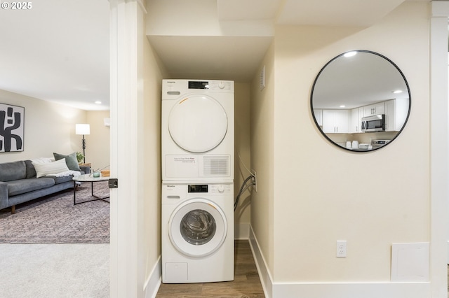 clothes washing area featuring baseboards, stacked washer and dryer, laundry area, and wood finished floors