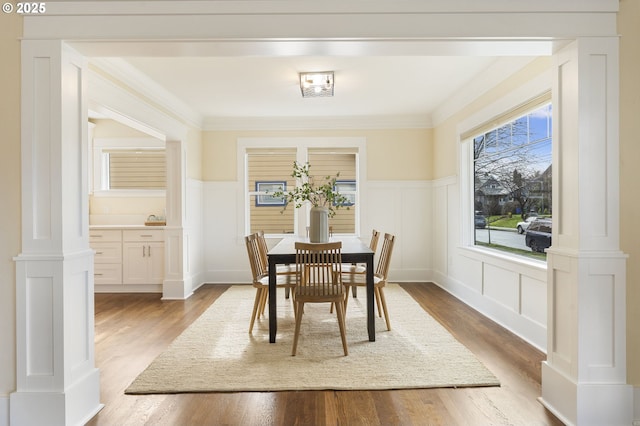 dining room with a decorative wall, a wainscoted wall, ornate columns, and crown molding