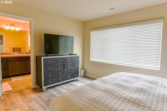 bedroom with light wood-style floors, visible vents, baseboards, and ensuite bathroom