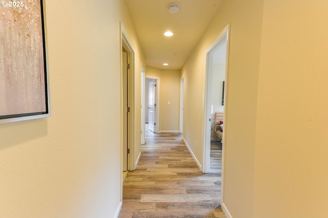 hall featuring baseboards, light wood finished floors, and recessed lighting