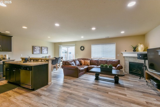 living room with a tiled fireplace, recessed lighting, and light wood-style flooring