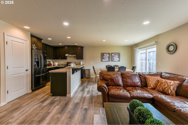 living room featuring a textured ceiling, baseboards, recessed lighting, and light wood-style floors
