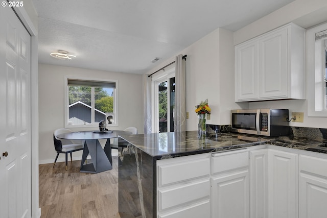 4634 Harriet Ave, Eugene, OR 97402 - kitchen featuring stainless steel microwave, white cabinets, light wood finished floors, and dark stone counters